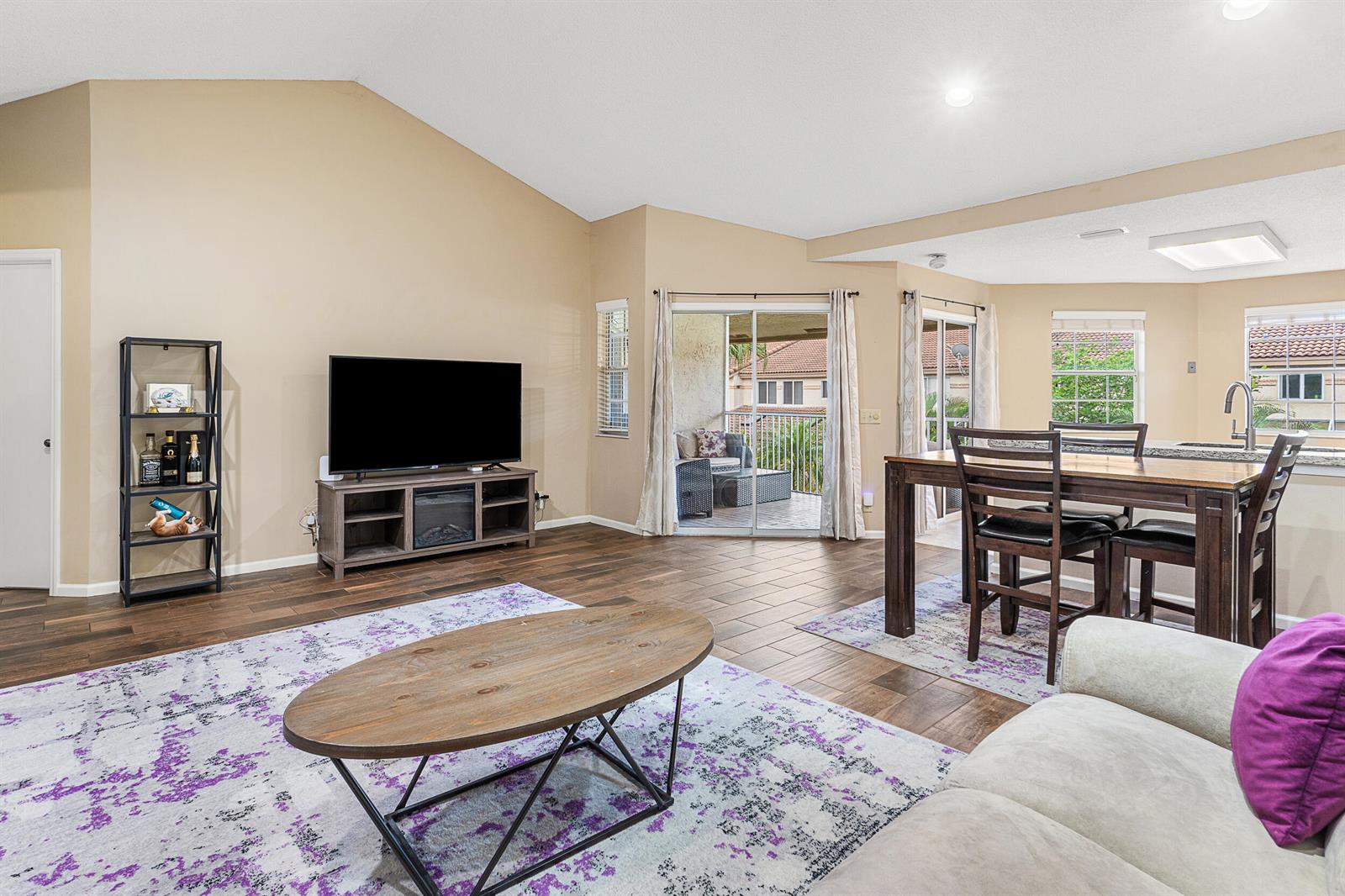 A living and dining area features wood-look tile flooring, a vaulted ceiling, and a balcony — 6626 Via Regina, Boca Raton FL 33433, BOCA RATON, FL