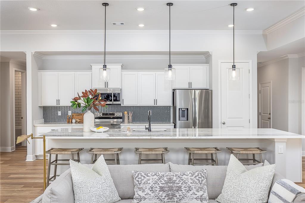 A modern kitchen features white cabinets, stainless steel appliances, a marble island, and bar seating — 16907 ROYAL PALM DRIVE, GROVELAND, FL