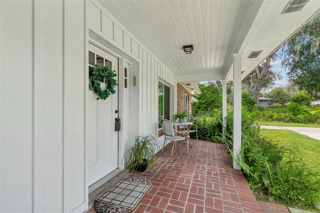 A covered porch features a red brick floor, white vertical siding, and a white front door — 909 TOMLINSON DRIVE, LUTZ, FL