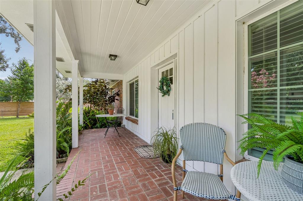A covered brick porch features white vertical siding, a front door, and outdoor patio furniture — 909 TOMLINSON DRIVE, LUTZ, FL