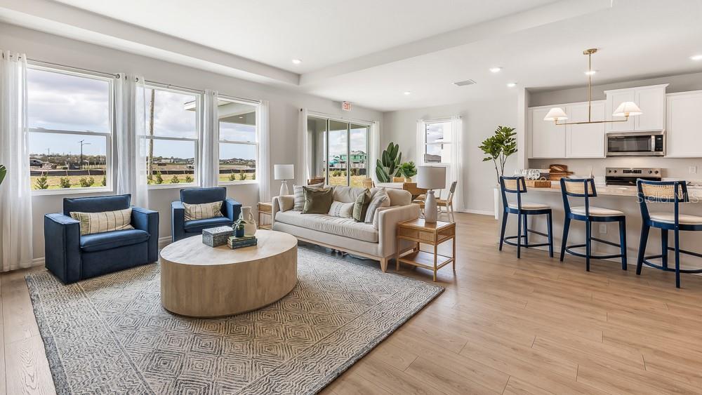 An open-concept living room and kitchen with light wood floors, white cabinets, and large windows — 18241 GANDER TERRACE, LAKEWOOD RANCH, FL