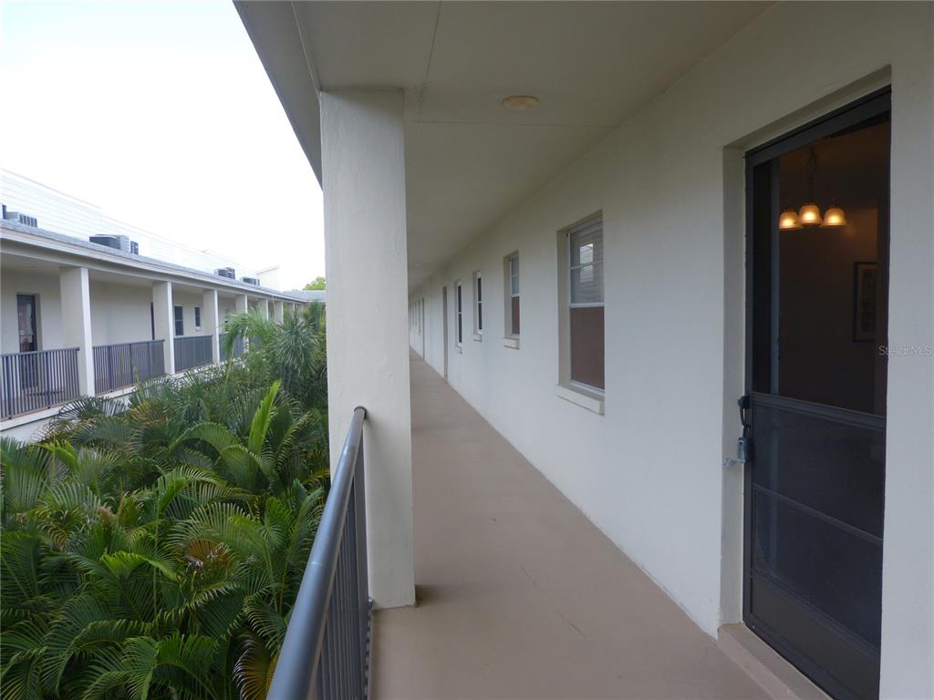 An outdoor walkway with a metal railing overlooks lush greenery beside a multi-story building — 2700 BAYSHORE BOULEVARD UNIT 5303, DUNEDIN, FL