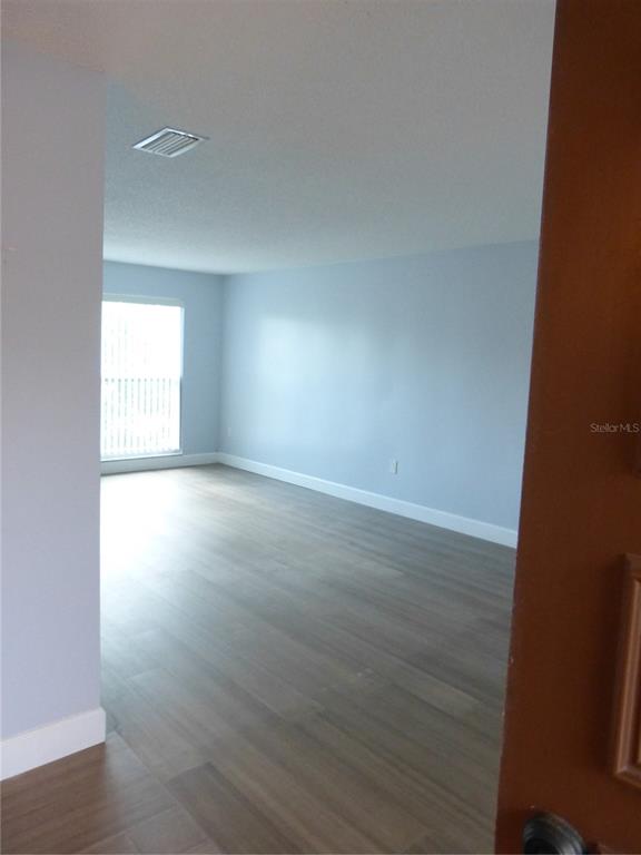 An empty room features light-colored wood-look flooring, light blue walls, and a window with blinds — 2700 BAYSHORE BOULEVARD UNIT 5303, DUNEDIN, FL