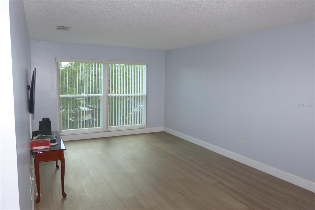 An empty room features light blue walls, wood-look flooring, and a large window with vertical blinds — 2700 BAYSHORE BOULEVARD UNIT 5303, DUNEDIN, FL
