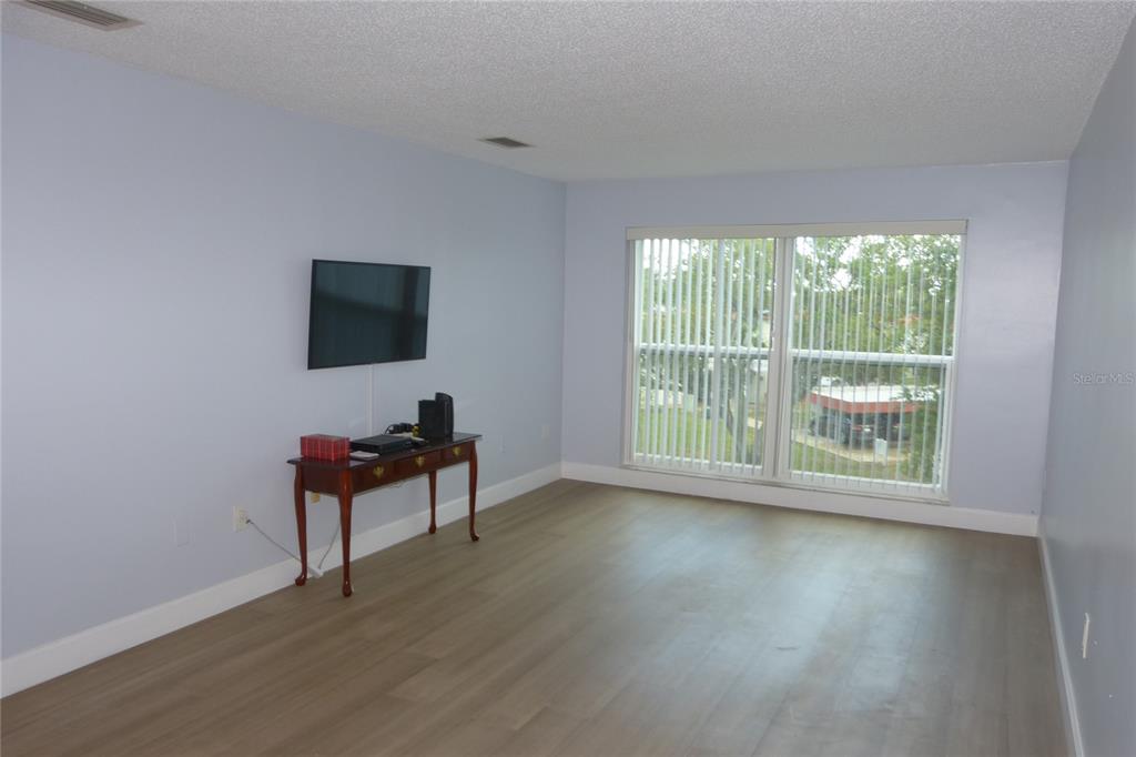 An empty living room features light blue walls, wood-look flooring, and a large window — 2700 BAYSHORE BOULEVARD UNIT 5303, DUNEDIN, FL