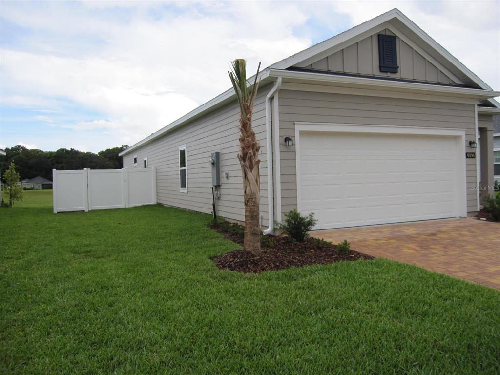 A side view of a single-story house with light siding, a two-car garage, and landscaping — 4494 NW 14TH LOOP, OCALA, FL