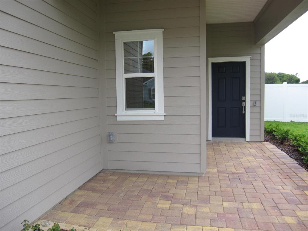A paved patio area features a dark door and a single window on beige siding — 4494 NW 14TH LOOP, OCALA, FL