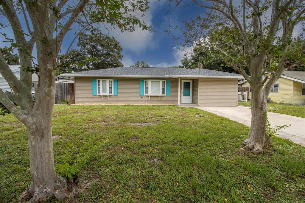A single-story house with tan siding, teal shutters, and a front lawn with two trees — 2865 POPLAR STREET, SARASOTA, FL