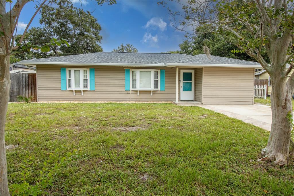 A single-story house with tan horizontal siding, bright blue shutters, and a front lawn — 2865 POPLAR STREET, SARASOTA, FL