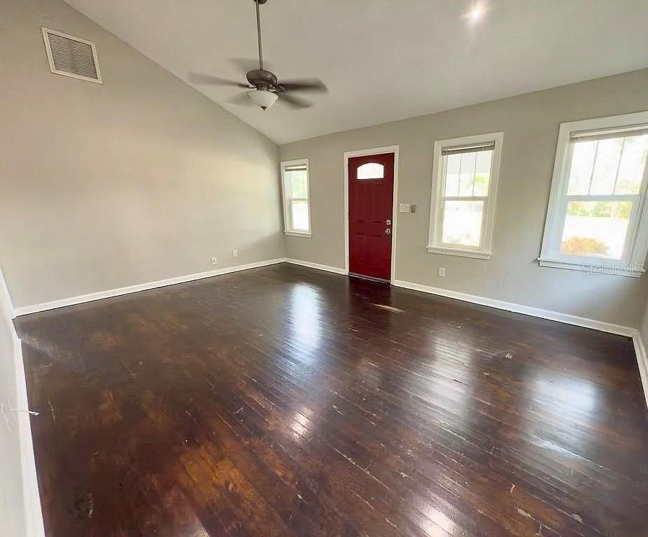 An empty living room features dark hardwood floors, a vaulted ceiling, and a red door — 2434 9TH AVENUE N, ST PETERSBURG, FL