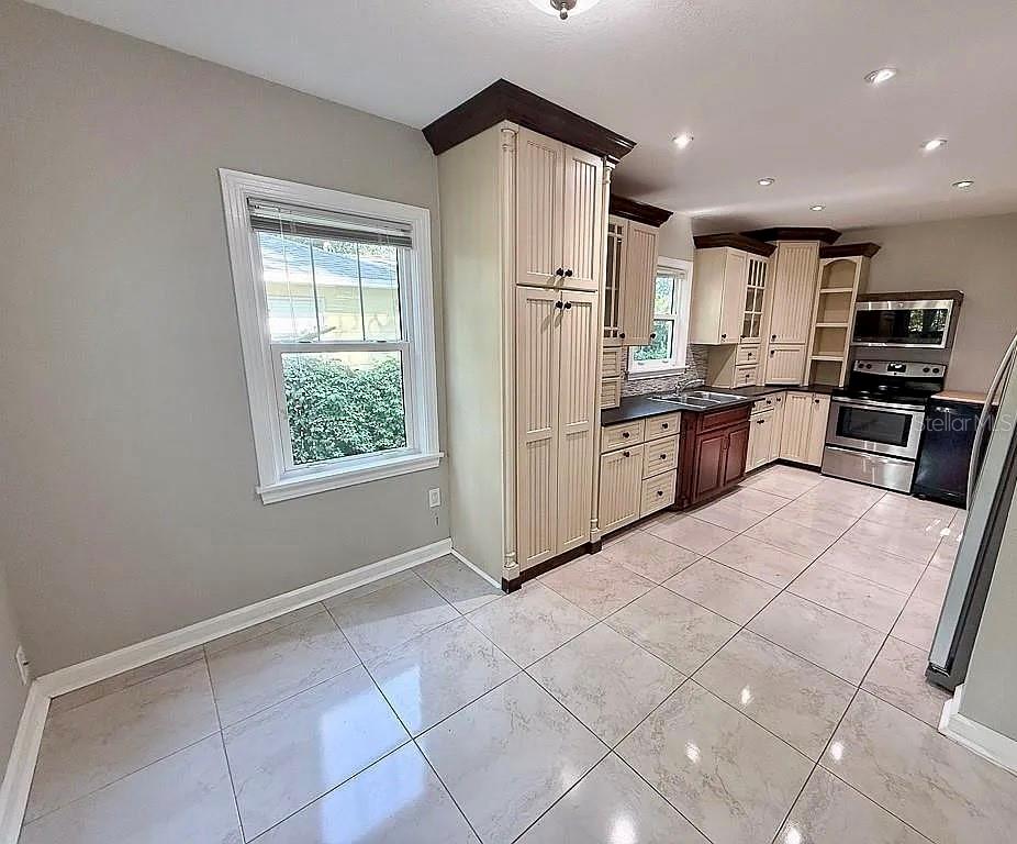 A kitchen with light-colored cabinets, dark wood accents, stainless steel appliances, and tiled flooring — 2434 9TH AVENUE N, ST PETERSBURG, FL