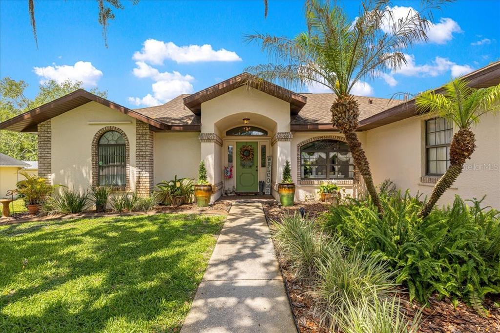 A single-story house with a light-colored stucco exterior, a green front door, and palm trees — 2964 S CYGNET TERRACE, INVERNESS, FL
