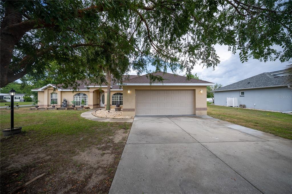 A single-story house with a beige stucco exterior, a two-car garage, and a concrete driveway — 6310 SW 82ND PLACE, OCALA, FL