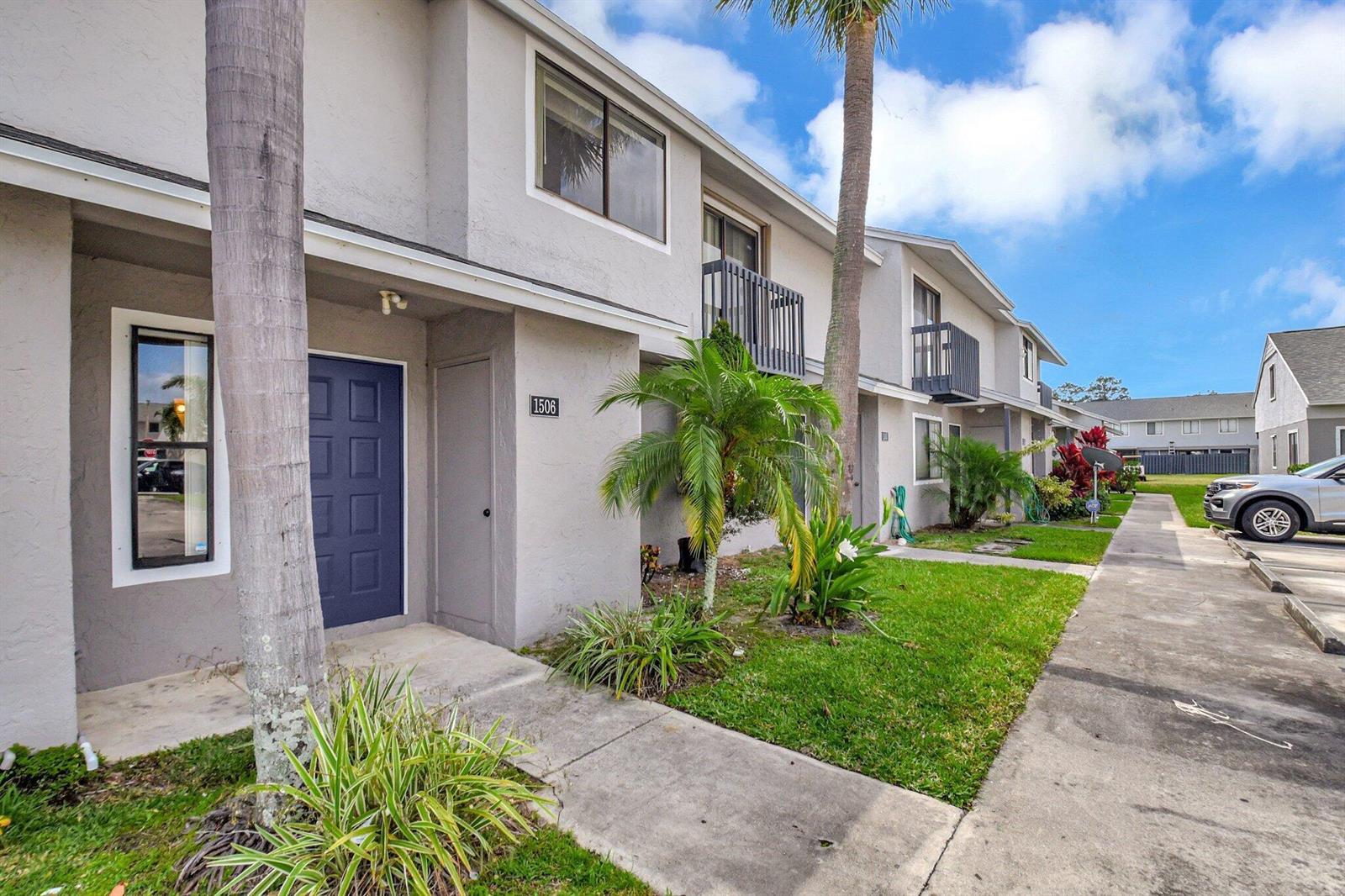 A two-story townhouse exterior with a blue front door, palm trees, and a concrete walkway — 1506 Wharf Lane, FL 33463, FL