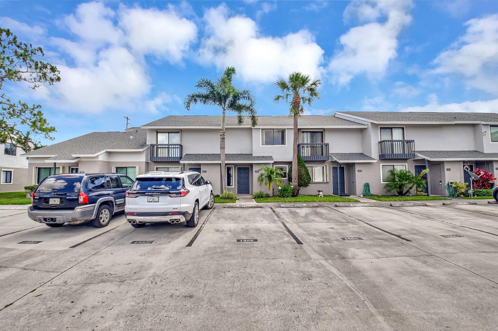 A two-story townhouse exterior with a concrete parking lot and two parked SUVs — 1506 Wharf Lane, FL 33463, FL