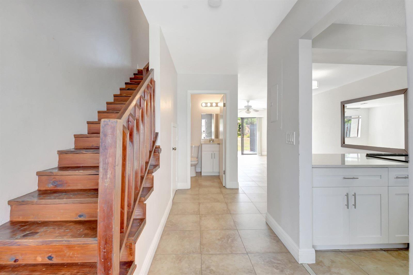 A hallway features a wooden staircase on the left, tiled flooring, and a bathroom ahead — 1506 Wharf Lane, FL 33463, FL