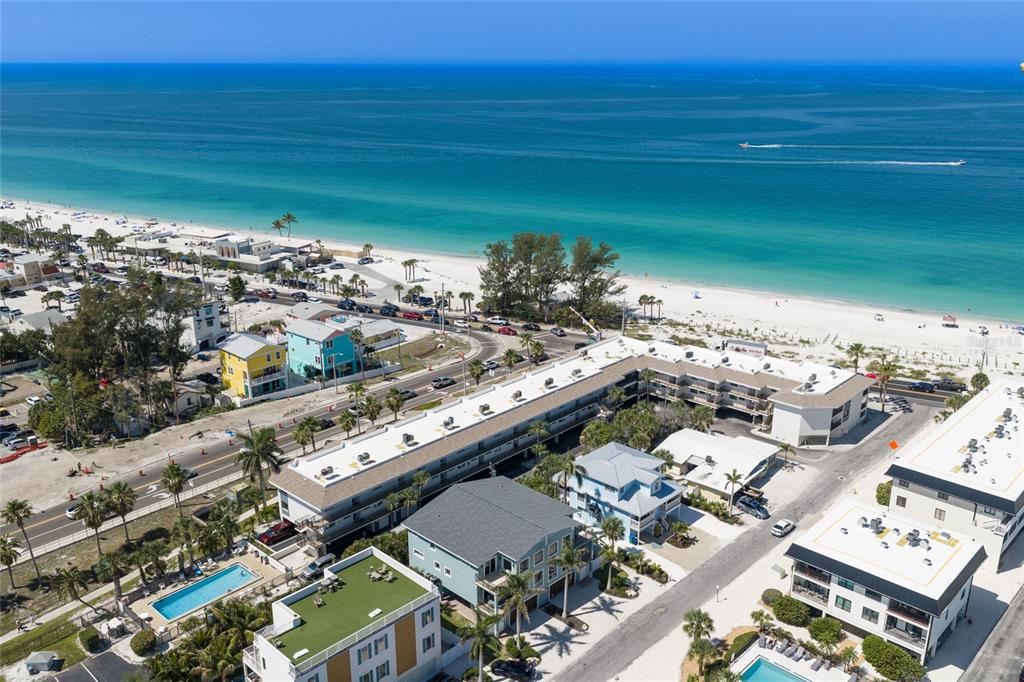 An aerial view shows a coastal neighborhood with multi-story buildings, a swimming pool, and beach — 109 6TH STREET N UNIT B, BRADENTON BEACH, FL