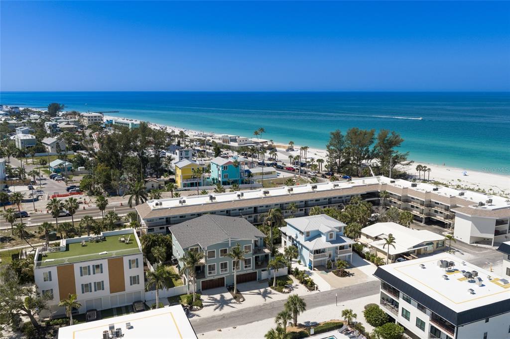 An aerial view shows a coastal neighborhood with multi-story buildings, palm trees, and a beach — 109 6TH STREET N UNIT B, BRADENTON BEACH, FL