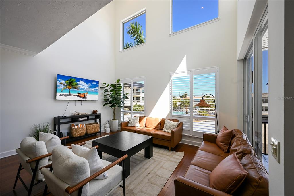 A living room with high ceilings, leather sofas, white armchairs, and large windows — 109 6TH STREET N UNIT B, BRADENTON BEACH, FL