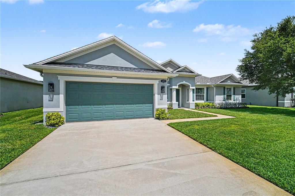 A single-story house with a teal garage door, gray stucco siding, and a concrete driveway — 1025 MORGAN CIRCLE NE, PALM BAY, FL