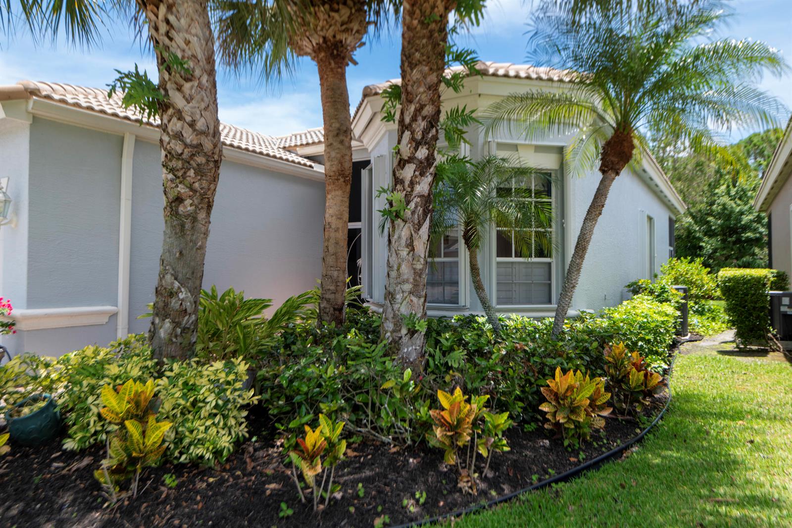 The exterior of a light-colored house features palm trees and a garden bed with crotons — 3785 NW Deer Oak Drive, Jensen Beach FL 34957, JENSEN BEACH, FL
