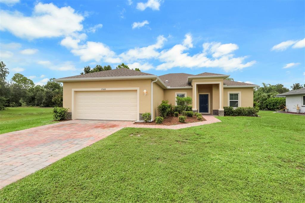 A single-story house with a tan stucco exterior, a two-car garage, and a paved walkway — 25108 PALISADE ROAD, PUNTA GORDA, FL