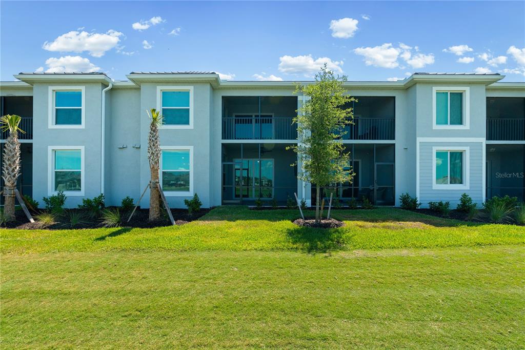 A two-story apartment building features screened-in balconies, light-colored siding, and a grassy lawn — 19015 SCALLOP LOOP UNIT 103, LAKEWOOD RANCH, FL