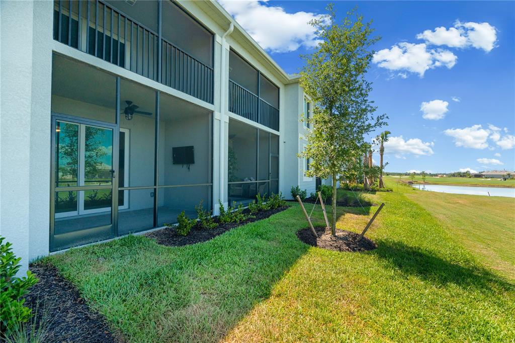 A two-story building features screened-in patios overlooking a grassy lawn and a small pond — 19015 SCALLOP LOOP UNIT 103, LAKEWOOD RANCH, FL