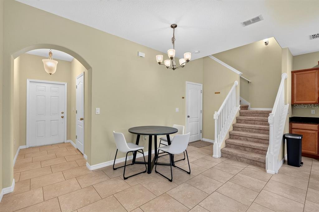 A dining area with a round table, white chairs, tile flooring, and a staircase — 205 WENTWORTH GRANDE DRIVE, DAYTONA BEACH, FL