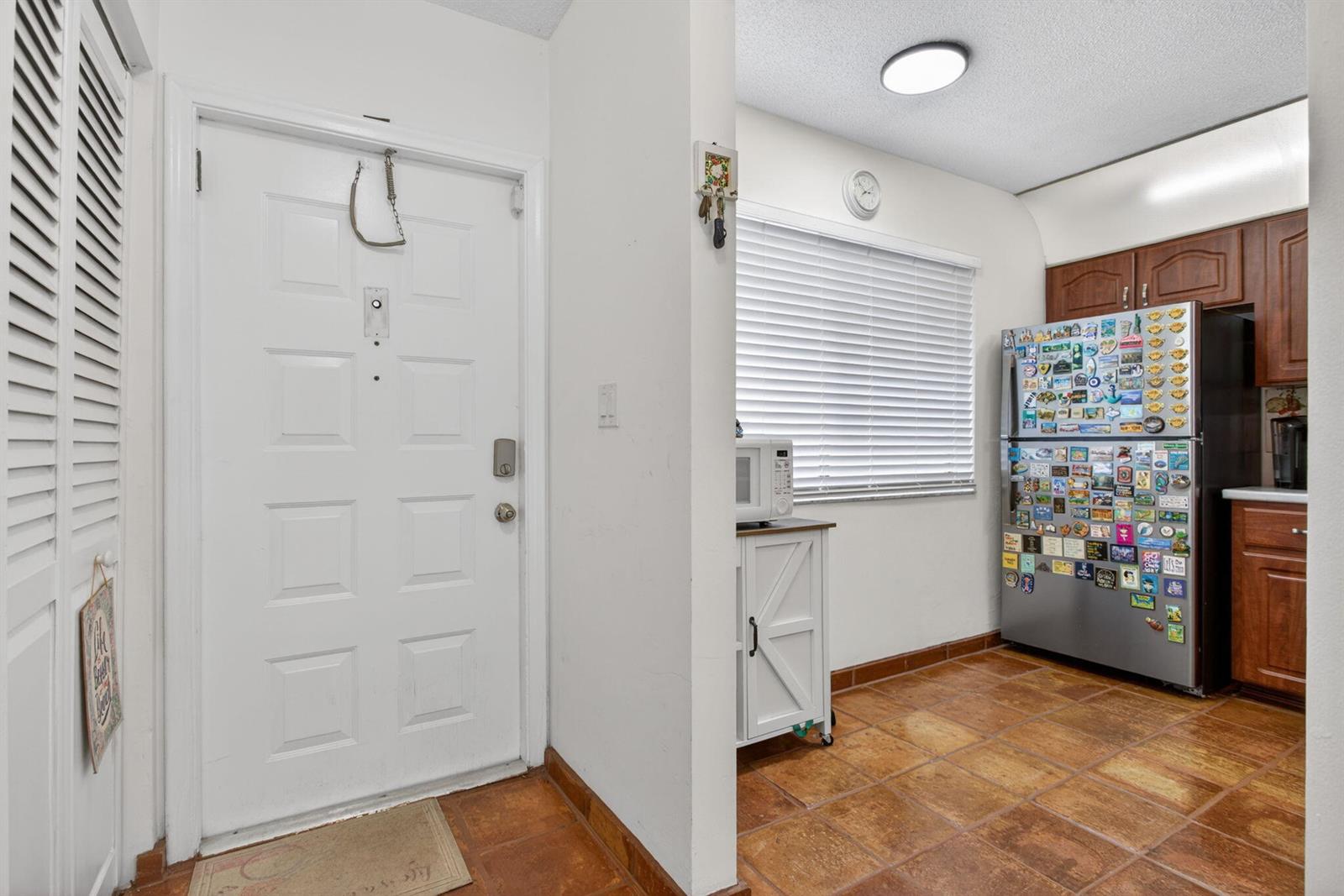 A kitchen entrance features a white door, tiled floors, a refrigerator, and wooden cabinets — 172 W Laurel Drive # 1102, Margate FL 33063, MARGATE, FL
