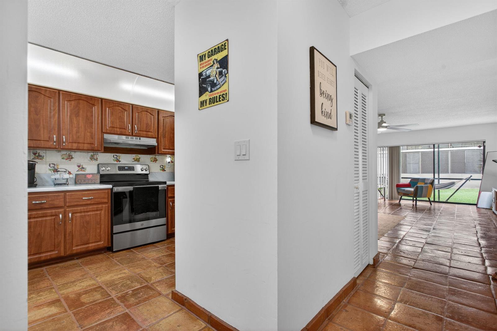 A kitchen with wood cabinets and tile floors opens to a living area with patio access — 172 W Laurel Drive # 1102, Margate FL 33063, MARGATE, FL