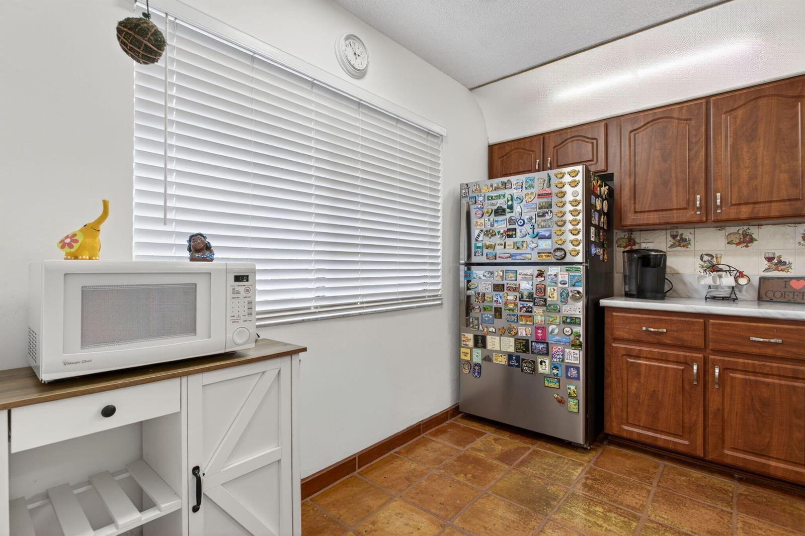 A kitchen features wood cabinets, a stainless steel refrigerator, a microwave, and tile flooring — 172 W Laurel Drive # 1102, Margate FL 33063, MARGATE, FL