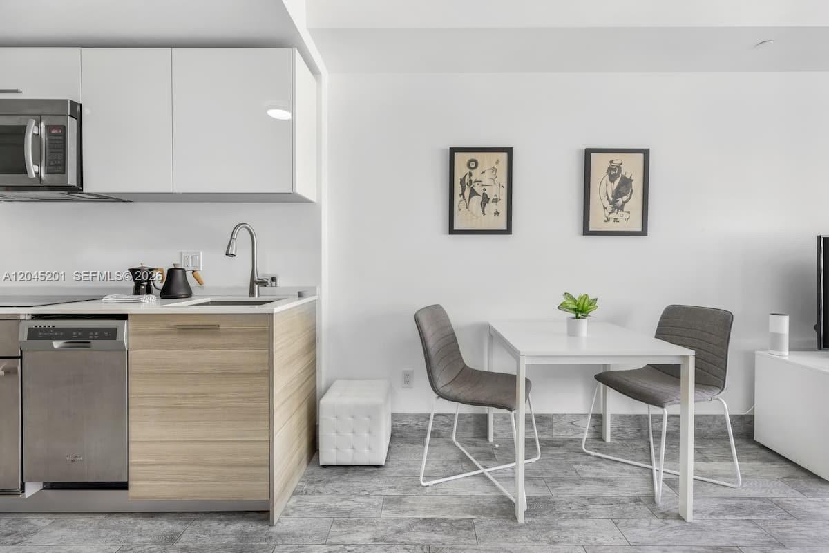 A modern kitchen features white cabinets, wood-tone lower cabinetry, and a small dining area — 1300 Brickell Bay Dr # 2713, Miami FL 33131, MIAMI, FL
