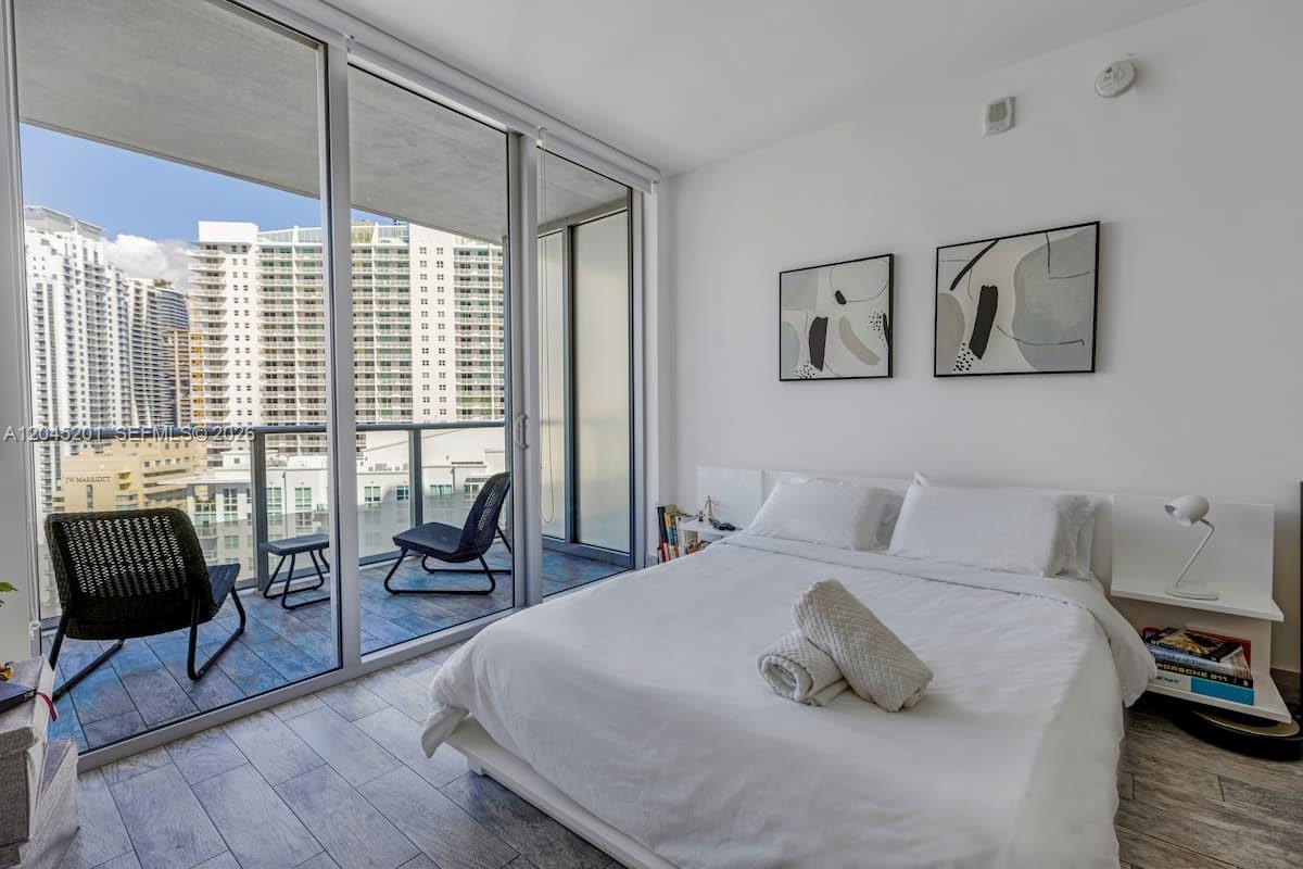 A bedroom features a white bed, abstract wall art, and a balcony with city views — 1300 Brickell Bay Dr # 2713, Miami FL 33131, MIAMI, FL