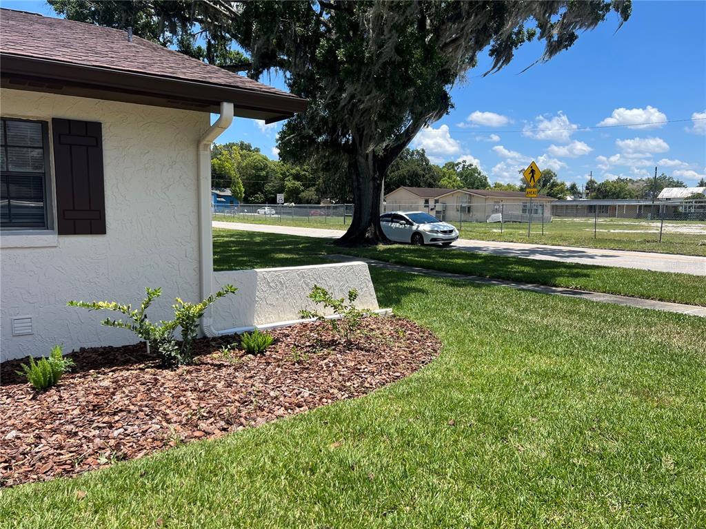 A white house exterior with brown shutters, a landscaped mulch bed, and a large tree — 937 MICHIGAN AVENUE, ST CLOUD, FL