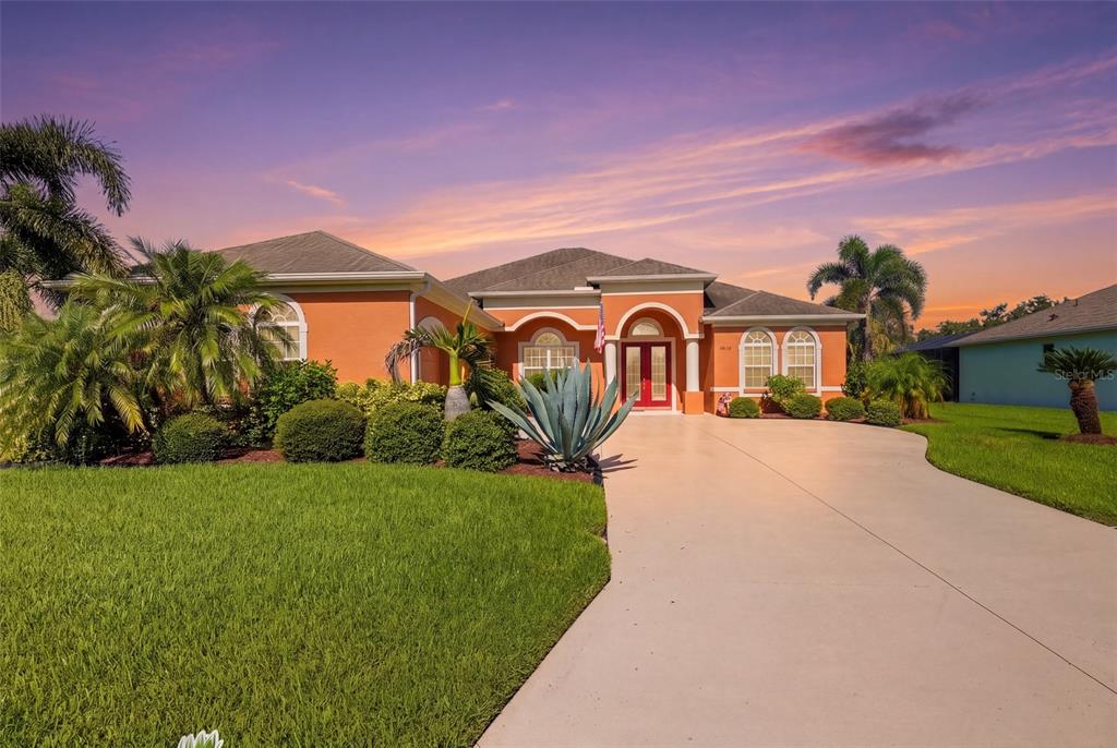 A single-story orange house with a concrete driveway and palm trees under a sunset sky — 12619 50TH COURT E, PARRISH, FL