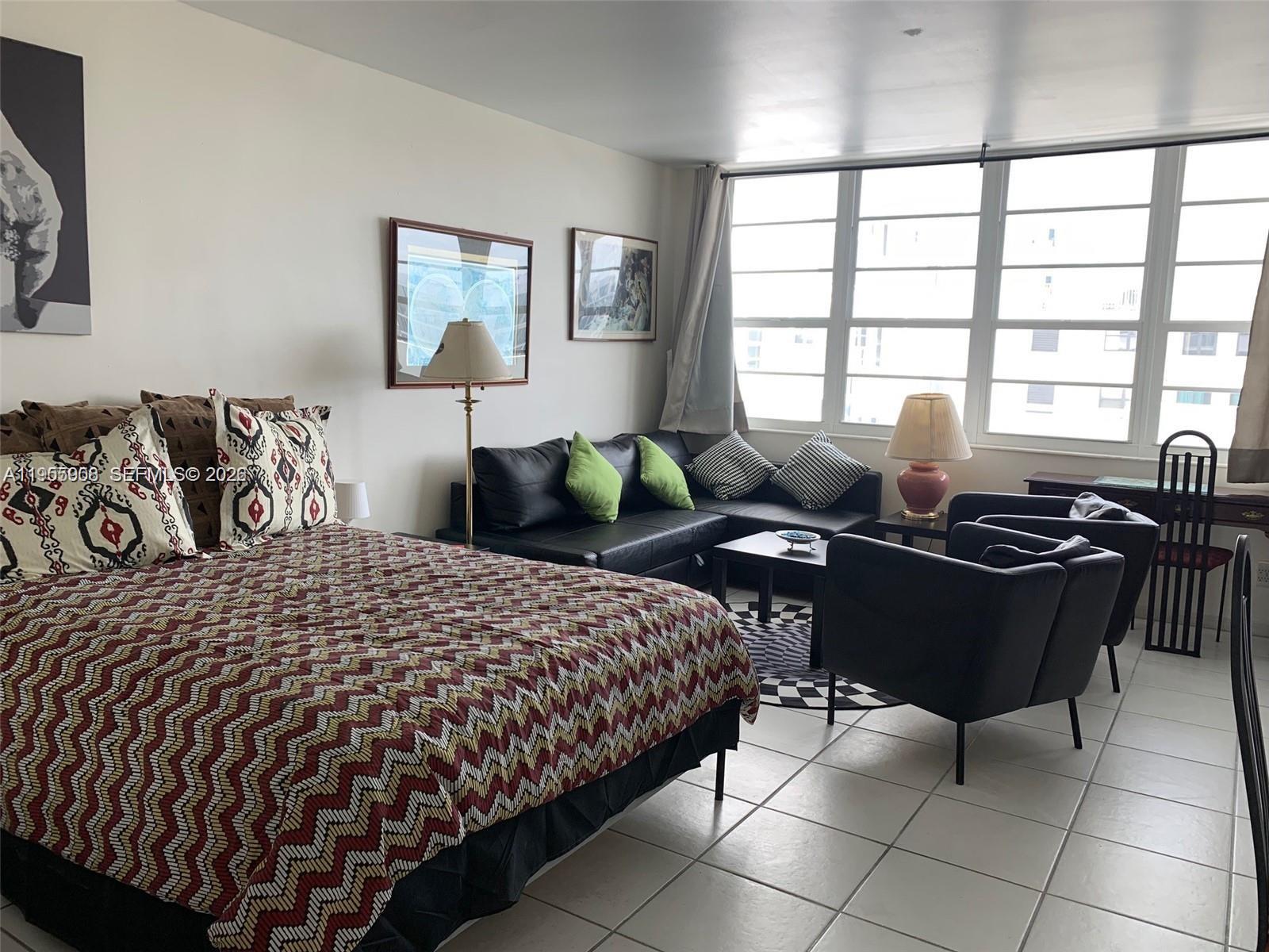 A bedroom with a bed, a black sectional sofa, two armchairs, and large windows — 100 Lincoln Rd # 903, Miami Beach FL 33139, MIAMI BEACH, FL