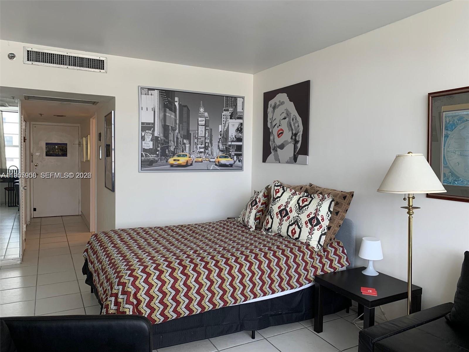 A bedroom features a bed with a patterned quilt, two wall art pieces, and a lamp — 100 Lincoln Rd # 903, Miami Beach FL 33139, MIAMI BEACH, FL