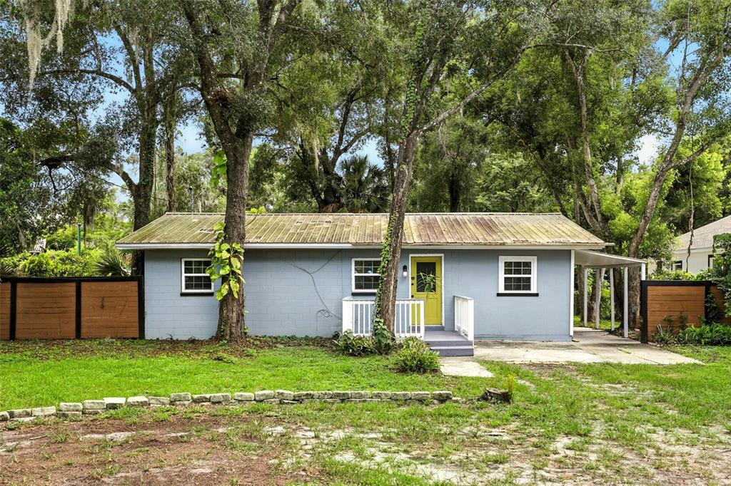 A single-story gray house with a yellow front door and a metal roof — 1412 E VOORHIS AVENUE, DELAND, FL