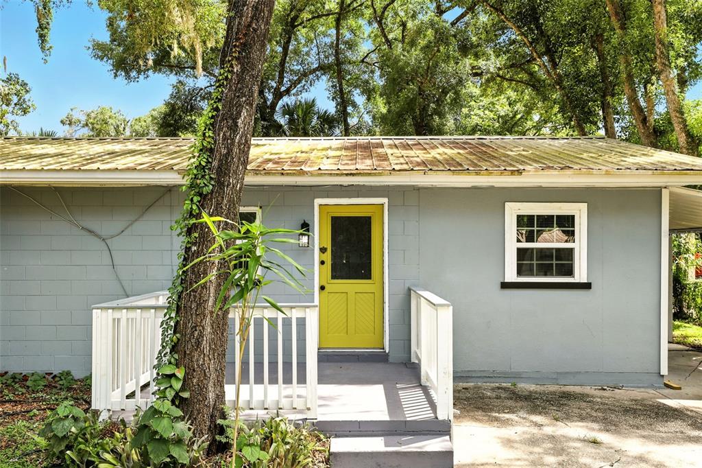 A gray concrete block house features a yellow front door, a white porch, and metal roof — 1412 E VOORHIS AVENUE, DELAND, FL