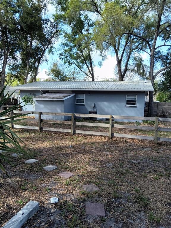 The exterior of a gray, single-story house with a metal roof sits behind a wooden fence — 1412 E VOORHIS AVENUE, DELAND, FL