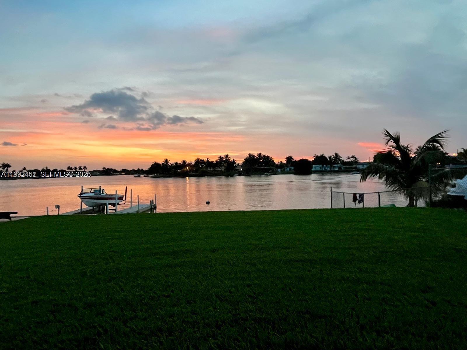 A grassy lawn overlooks a calm waterway with a boat lift at sunset — 18400 NW 78th Ave, Hialeah FL 33015, HIALEAH, FL