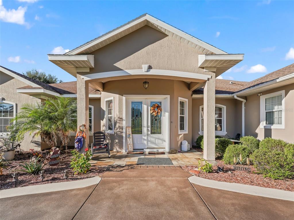 The exterior of a tan house features a covered entryway with double doors and landscaping — 9926 SE SUNSET HARBOR ROAD, SUMMERFIELD, FL