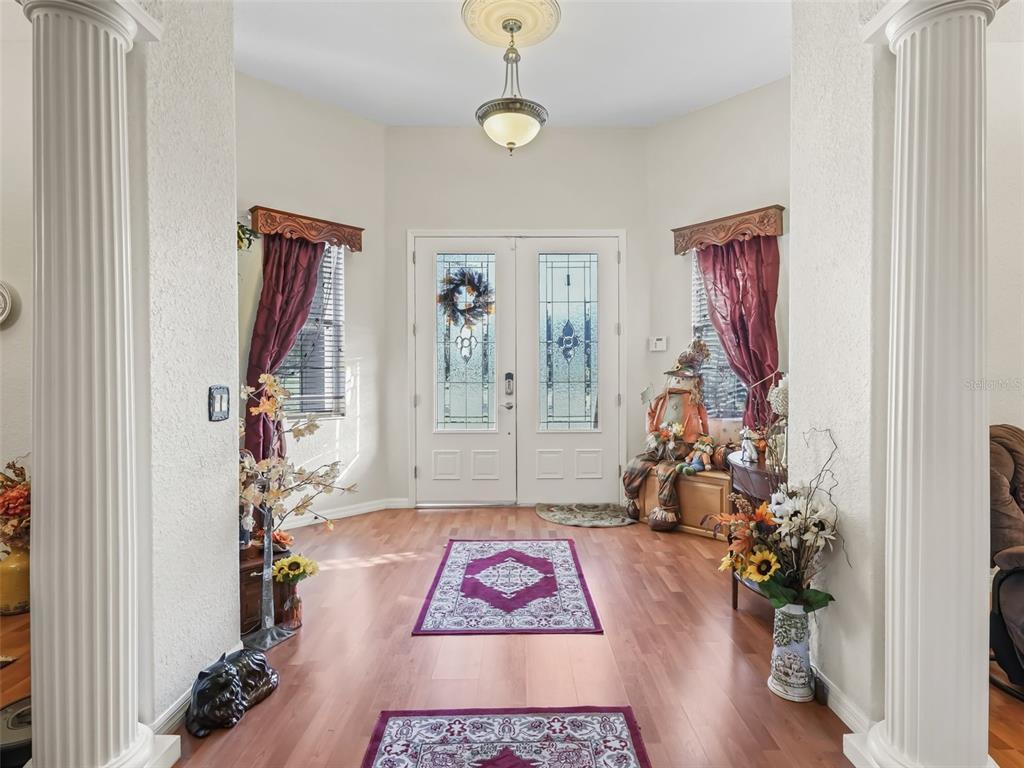 A bright entryway features wood flooring, white columns, double glass-paneled doors, and decorative rugs — 9926 SE SUNSET HARBOR ROAD, SUMMERFIELD, FL