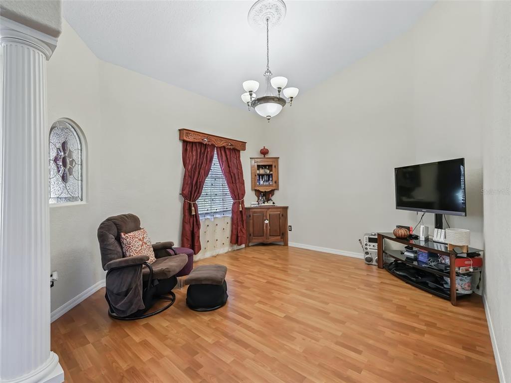 A living room features wood-look flooring, a ceiling chandelier, a recliner, and a television stand — 9926 SE SUNSET HARBOR ROAD, SUMMERFIELD, FL