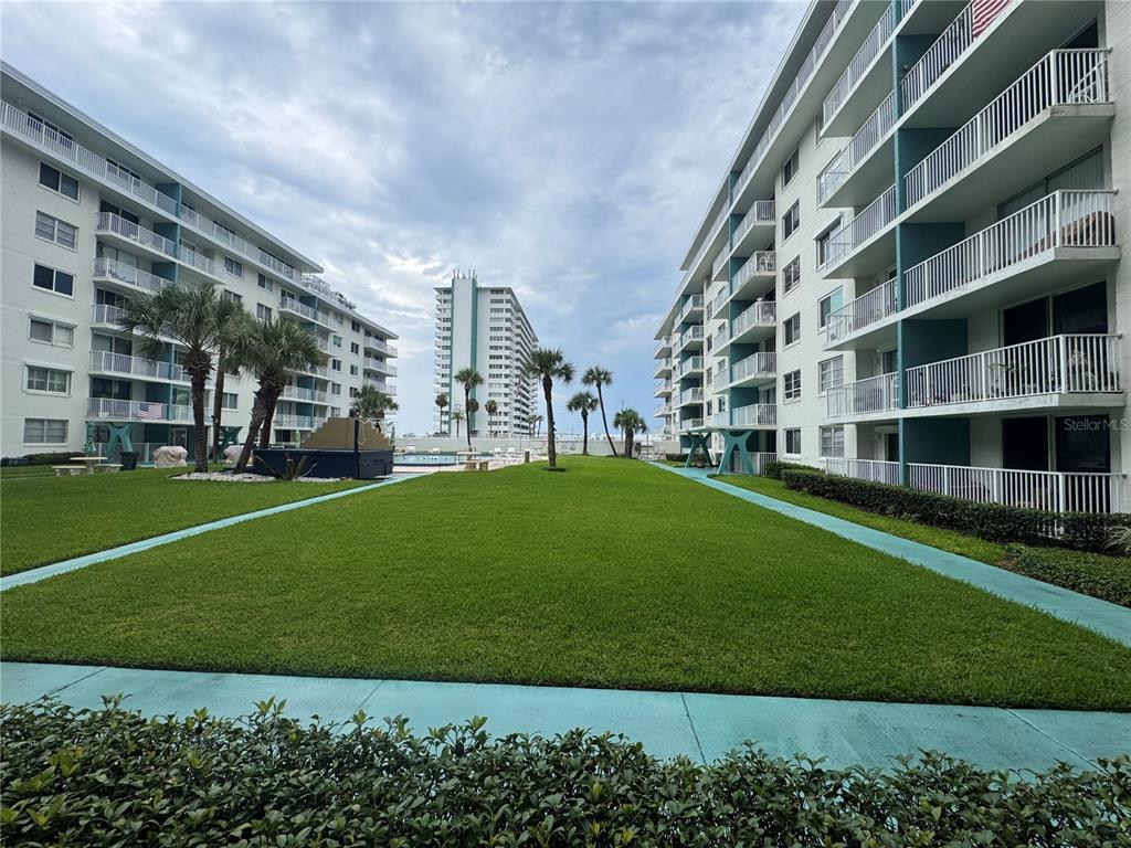 A grassy courtyard sits between two multi-story apartment buildings with balconies under a cloudy sky — 2727 N ATLANTIC AVENUE UNIT 110, DAYTONA BEACH, FL