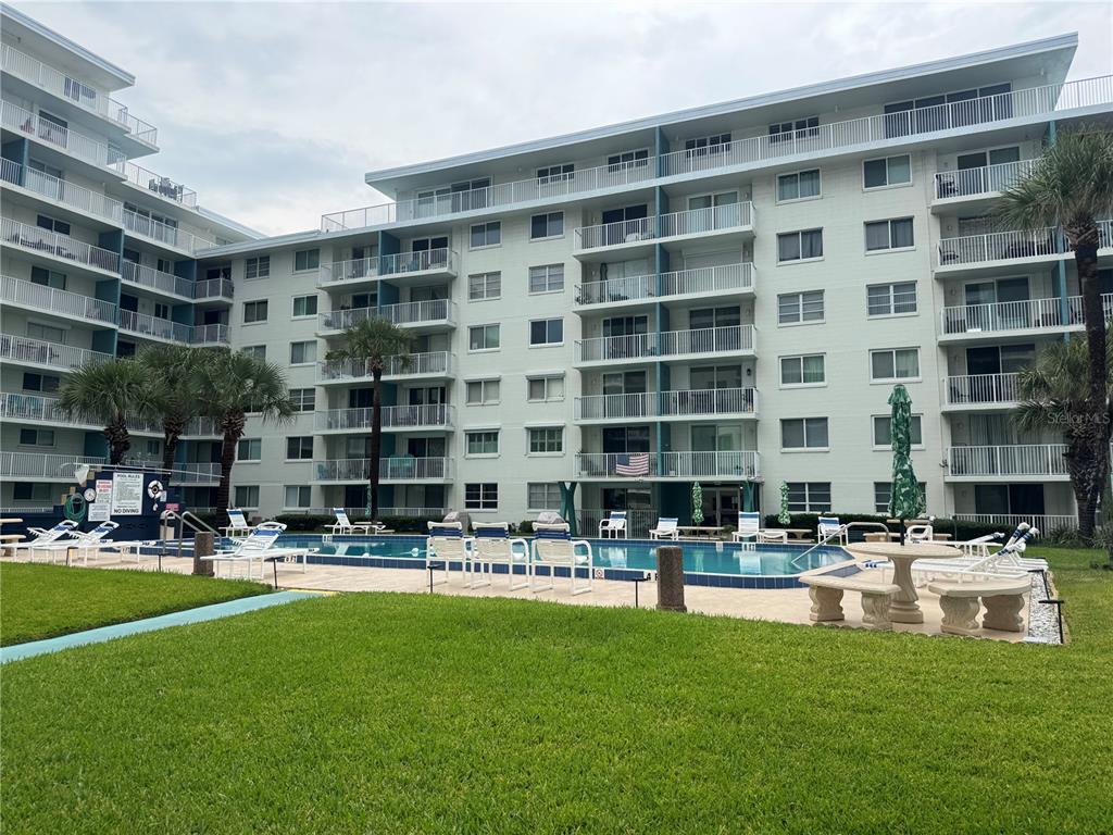 A multi-story apartment building with balconies overlooks a swimming pool and a grassy lawn — 2727 N ATLANTIC AVENUE UNIT 110, DAYTONA BEACH, FL