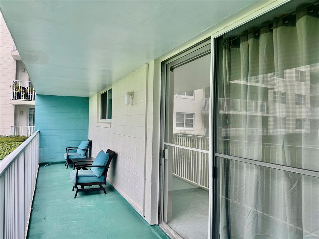 A balcony with a teal floor, two chairs, and a sliding glass door — 2727 N ATLANTIC AVENUE UNIT 110, DAYTONA BEACH, FL