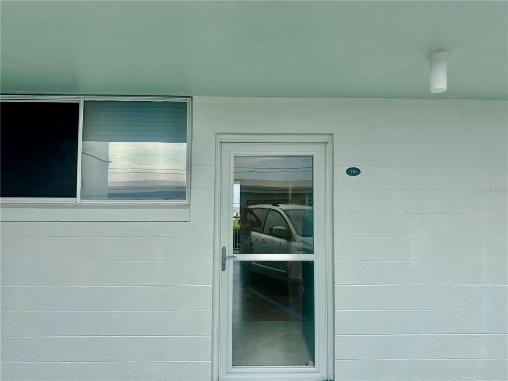 A white exterior wall features a glass storm door and a window with blinds — 2727 N ATLANTIC AVENUE UNIT 110, DAYTONA BEACH, FL