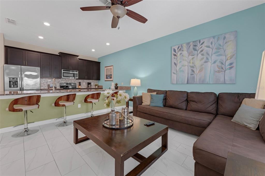 A living room and kitchen area with dark cabinets, a brown sectional, and tiled floors — 4805 BRIER ROSE LANE, KISSIMMEE, FL